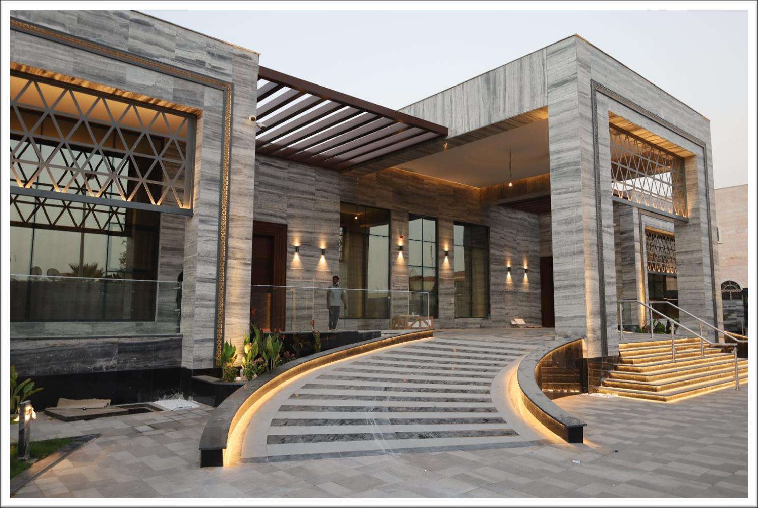 Private villa entrance at dusk with lit pergola and glass façade
